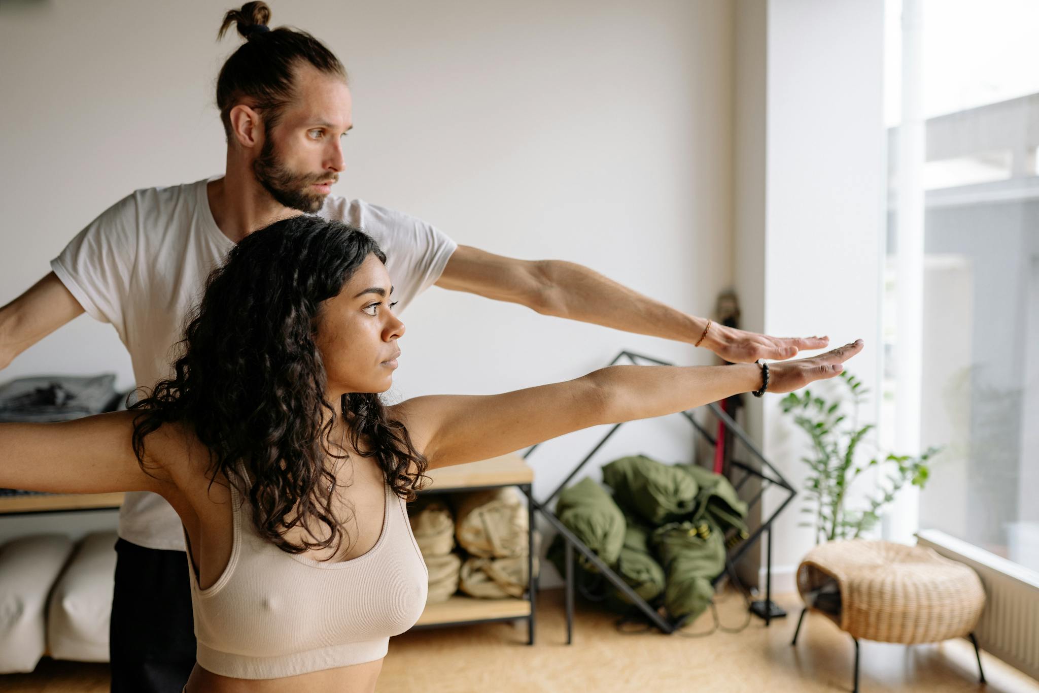 A yoga instructor helps a woman with her Warrior Pose in a serene indoor studio.