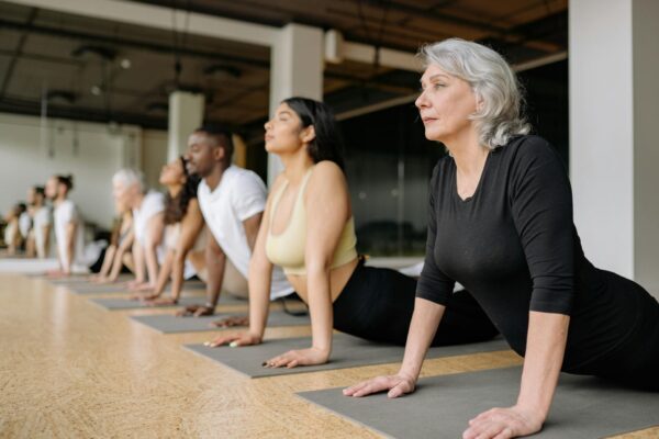 A diverse group of adults in a yoga class, practicing stretching on mats indoors.